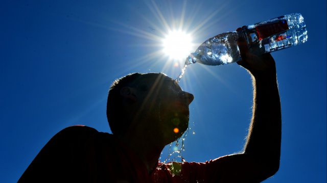 Sous un soleil de plomb, Homme se versant de l'eau en bouteille sur la tête pour se rafraîchir